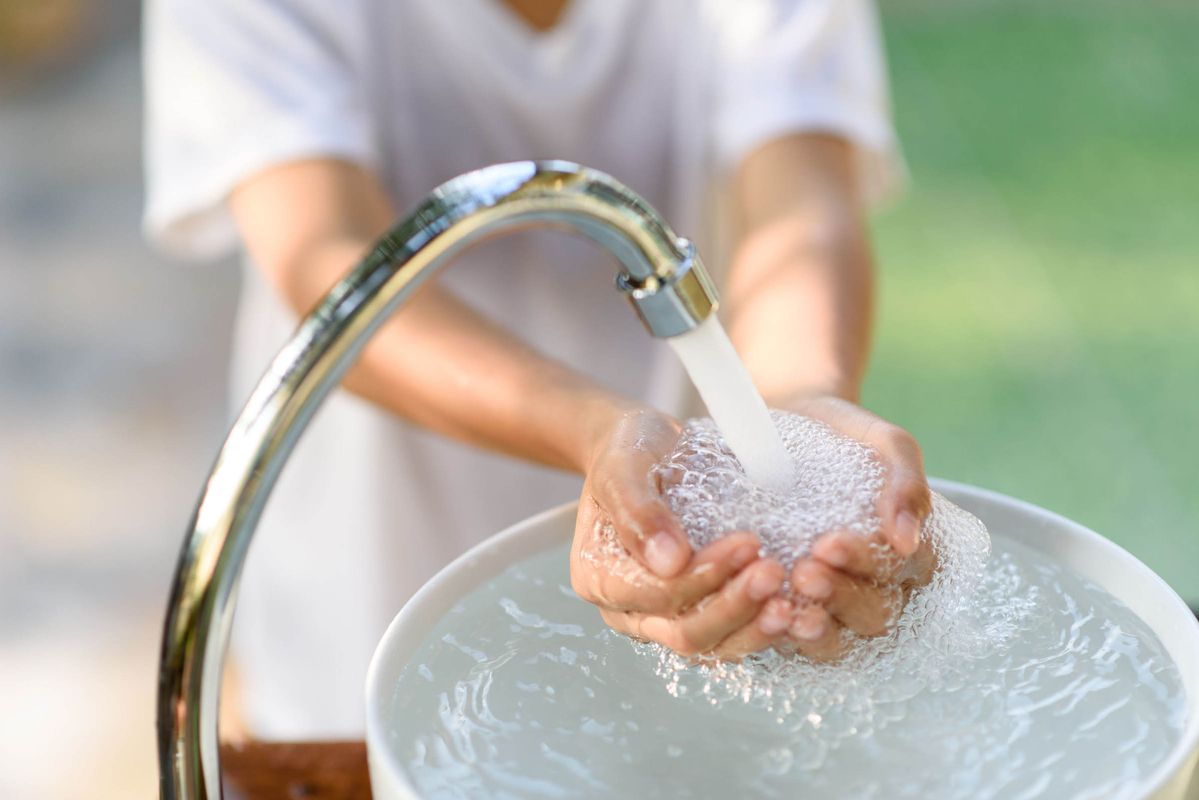 Wasserhahn strahlt Wasser in offene Kinderhände